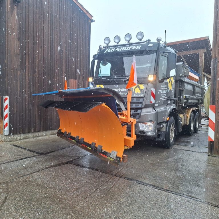 Ein Lastwagen mit Schneeschippe dran im Winter vor einer Scheune